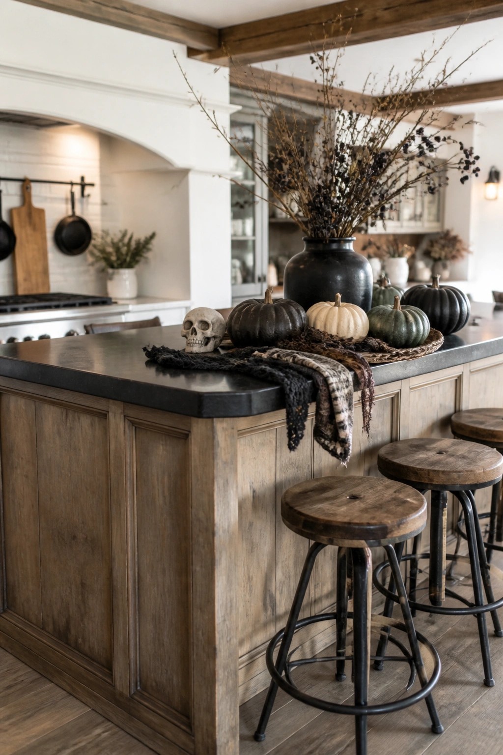 Kitchen island with a decorative skull, black and dark green pumpkins, and a large vase of bare branches on a dark countertop.