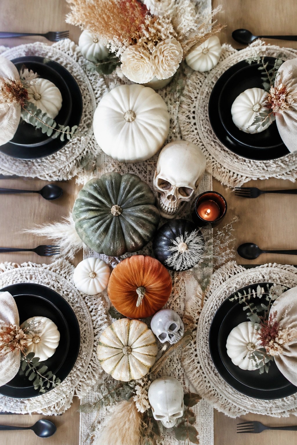 Dining table set with black plates, white and painted pumpkins, multiple skulls, and dried flowers as a Halloween centerpiece.
