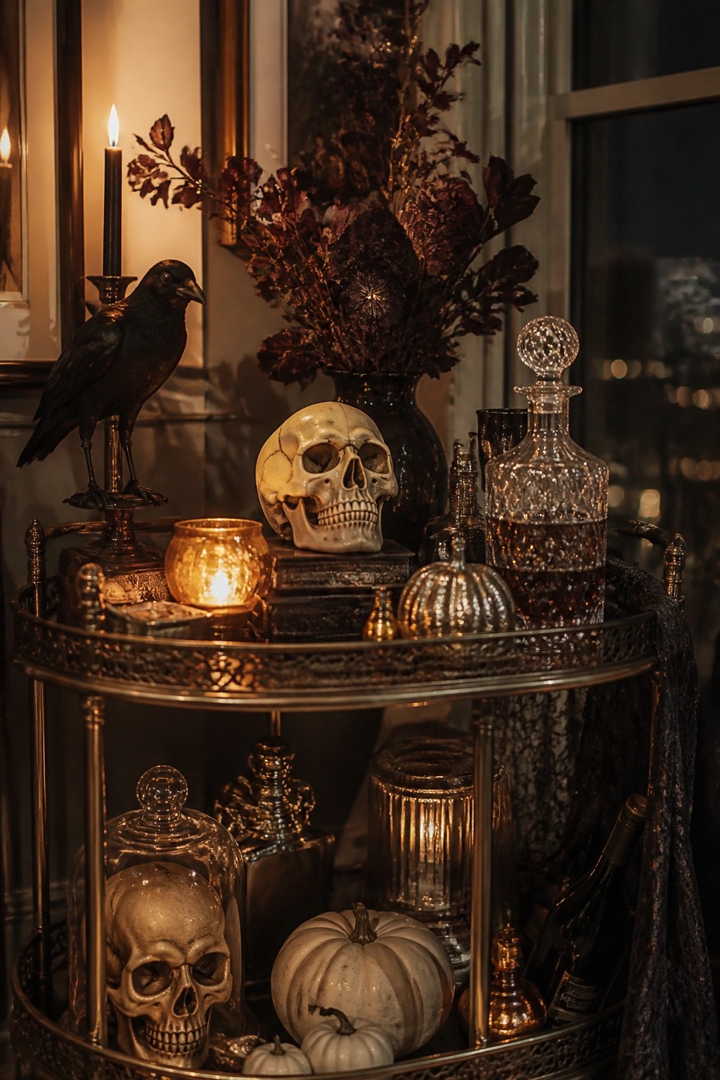 A metallic bar cart styled with multiple skulls, a black crow figure, dark dried foliage, candles, and small white pumpkins.
