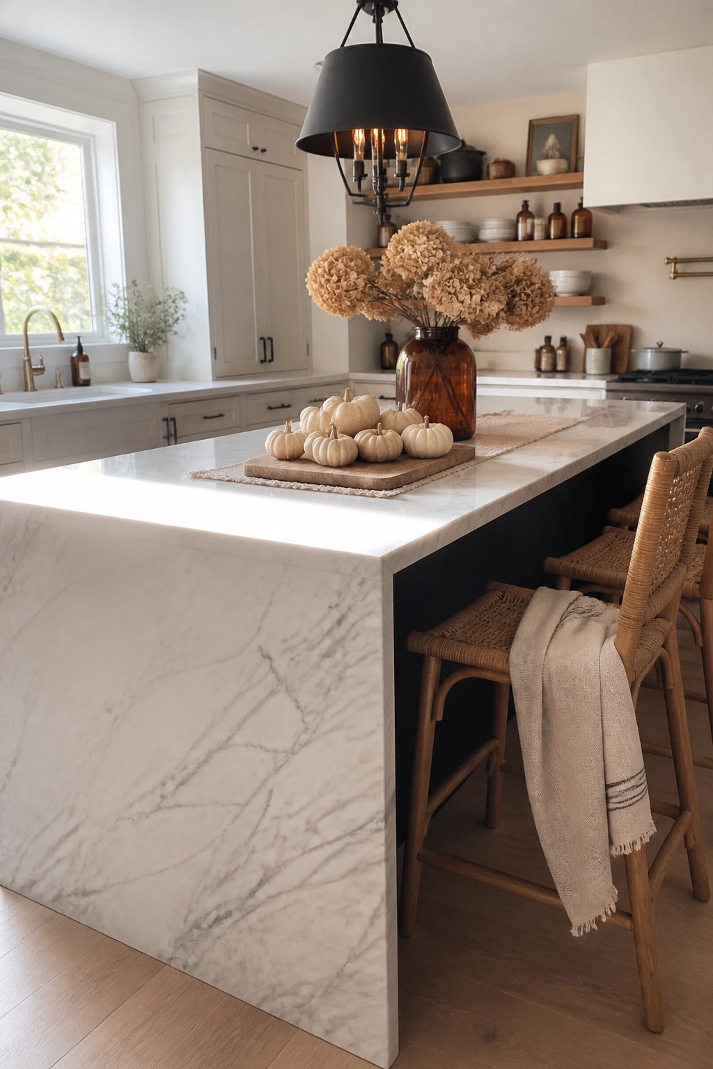 White marble kitchen island with pumpkins, dried hydrangeas, woven stools, and black pendant light