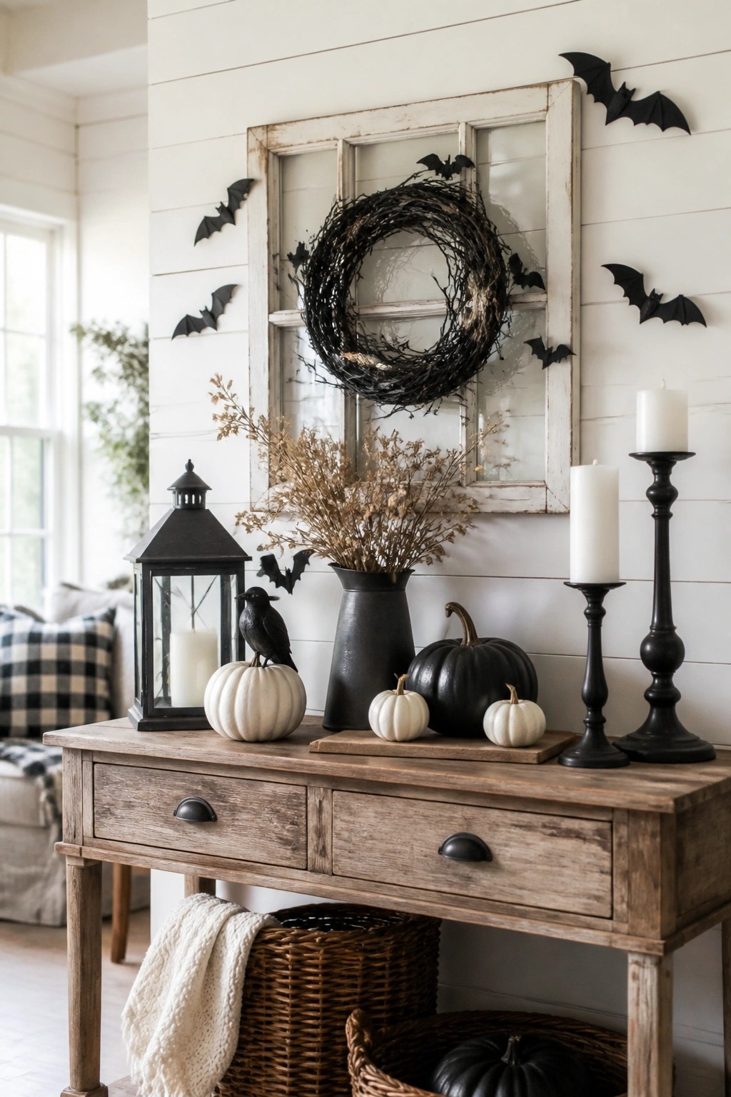 White entryway wall with black bats arranged around a black wreath on a large distressed window frame above a wooden console table.
