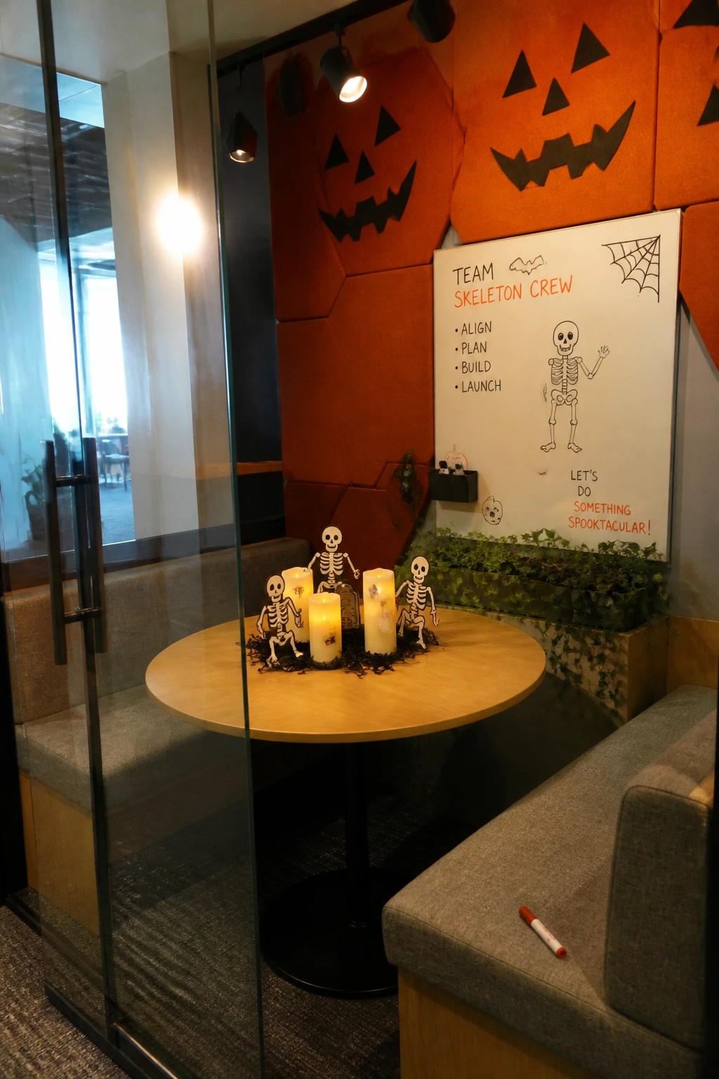 Office nook with skeleton figurines, candles on round table, pumpkin wall and whiteboard.