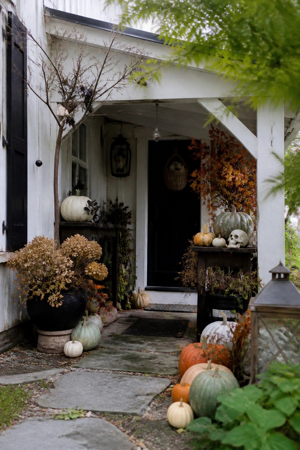 Rustic white farmhouse porch with pumpkins and a skull arranged on a dark wooden table beside the front door.