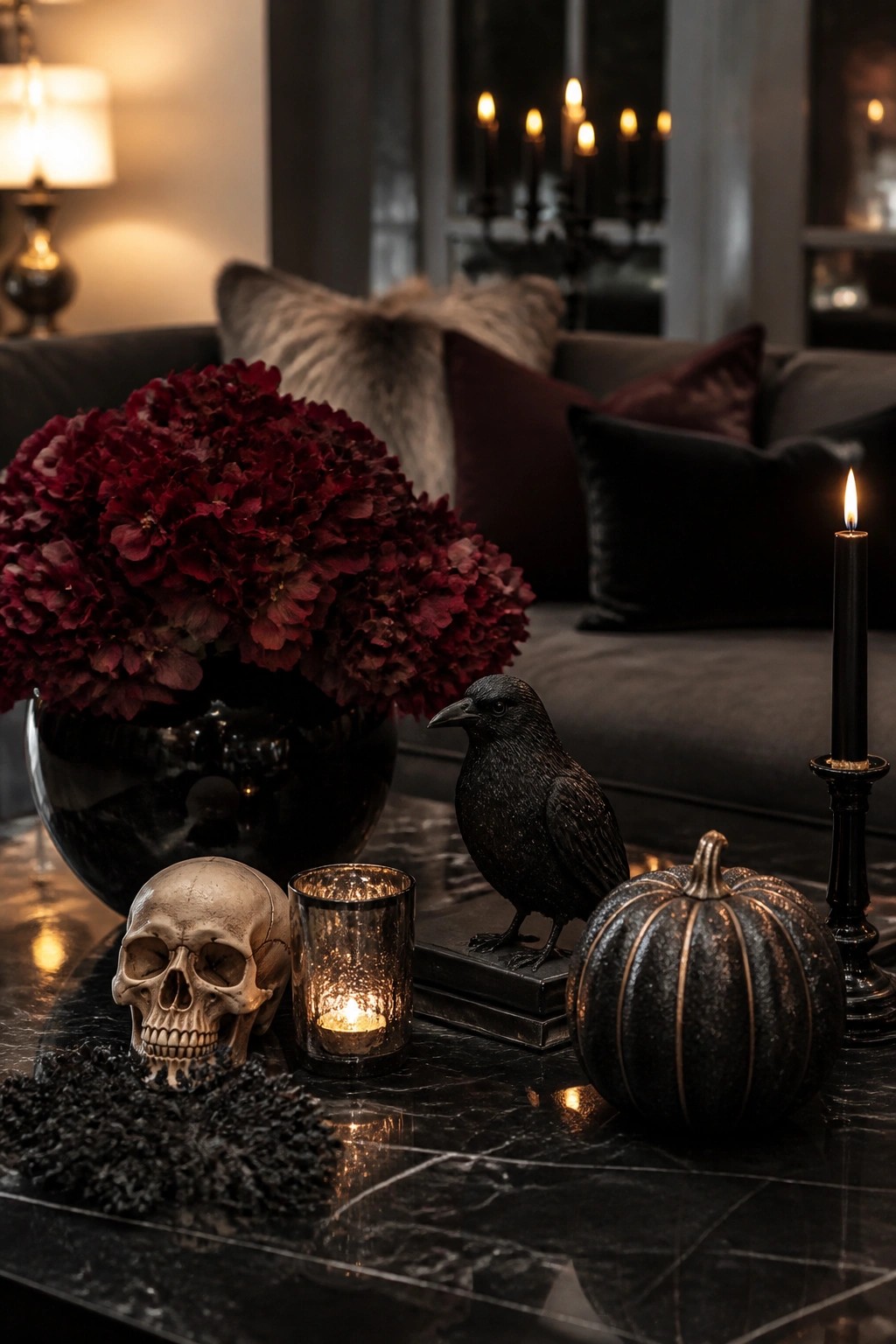 Living room coffee table with a skull, black crow statue on books, black pumpkin, and lit candles arranged on a marble surface.