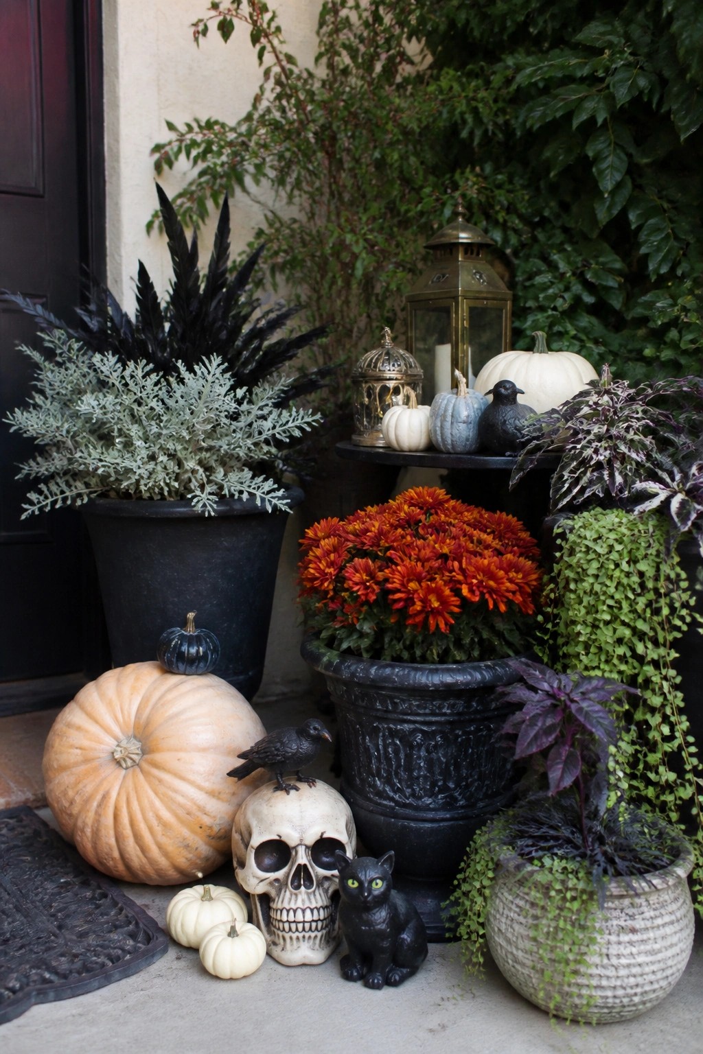 Front porch entrance with a large decorative skull, black cat figurine, crow, and assorted pumpkins arranged beside potted plants.