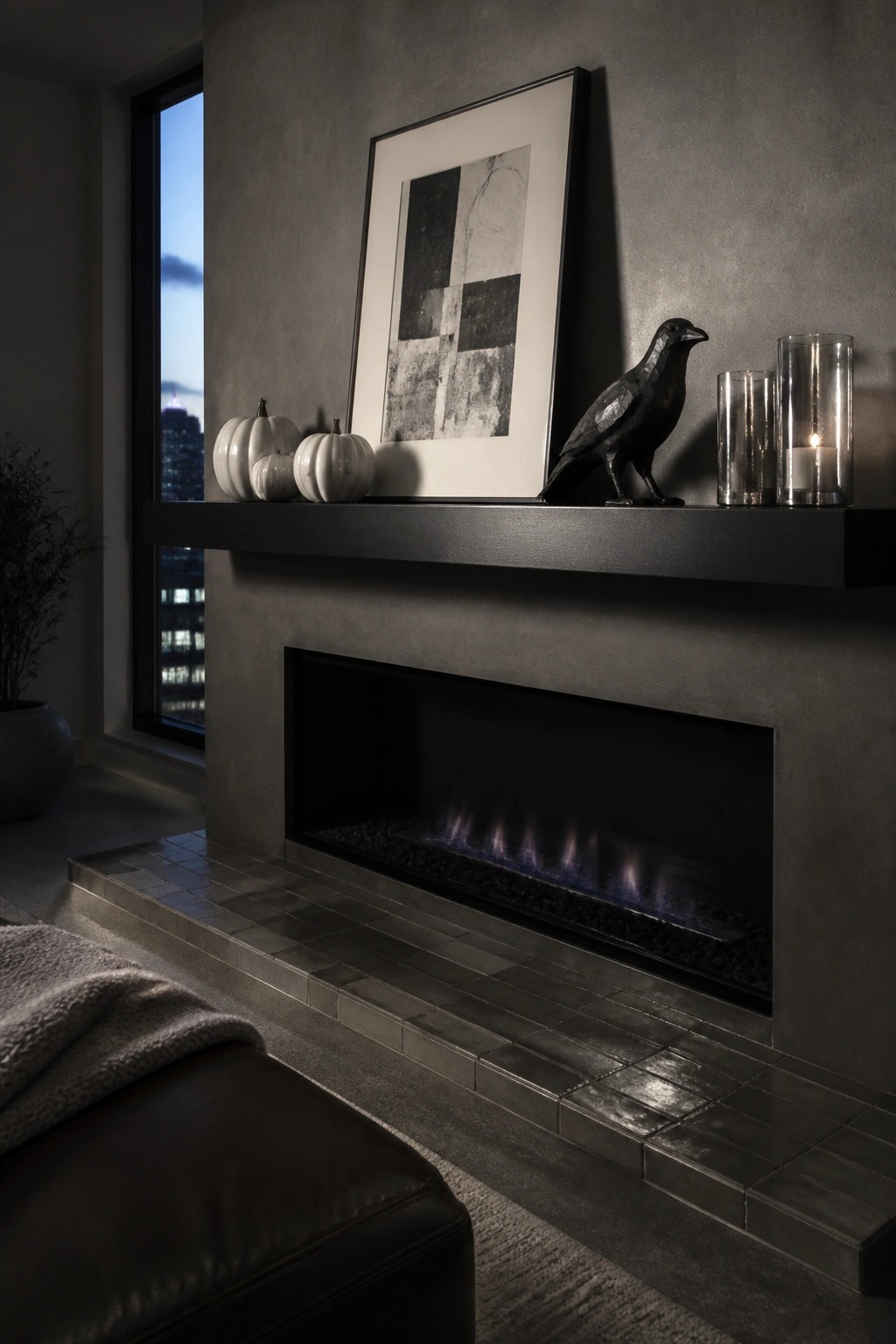A modern fireplace with a long black mantel holding white pumpkins, a black bird statue, framed abstract art, and glass candle holders.