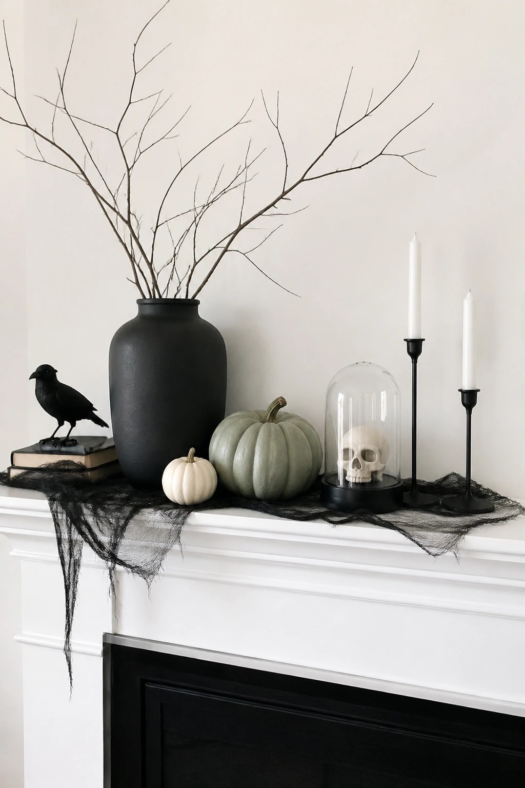 White fireplace mantel decorated with a black vase holding bare branches, a skull under glass, a black crow figurine, pumpkins, and black netting.