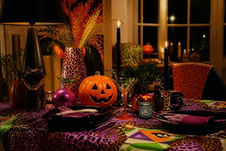 Lavish Halloween table with carved pumpkins, lit candles, colorful glassware, and zebra plates
