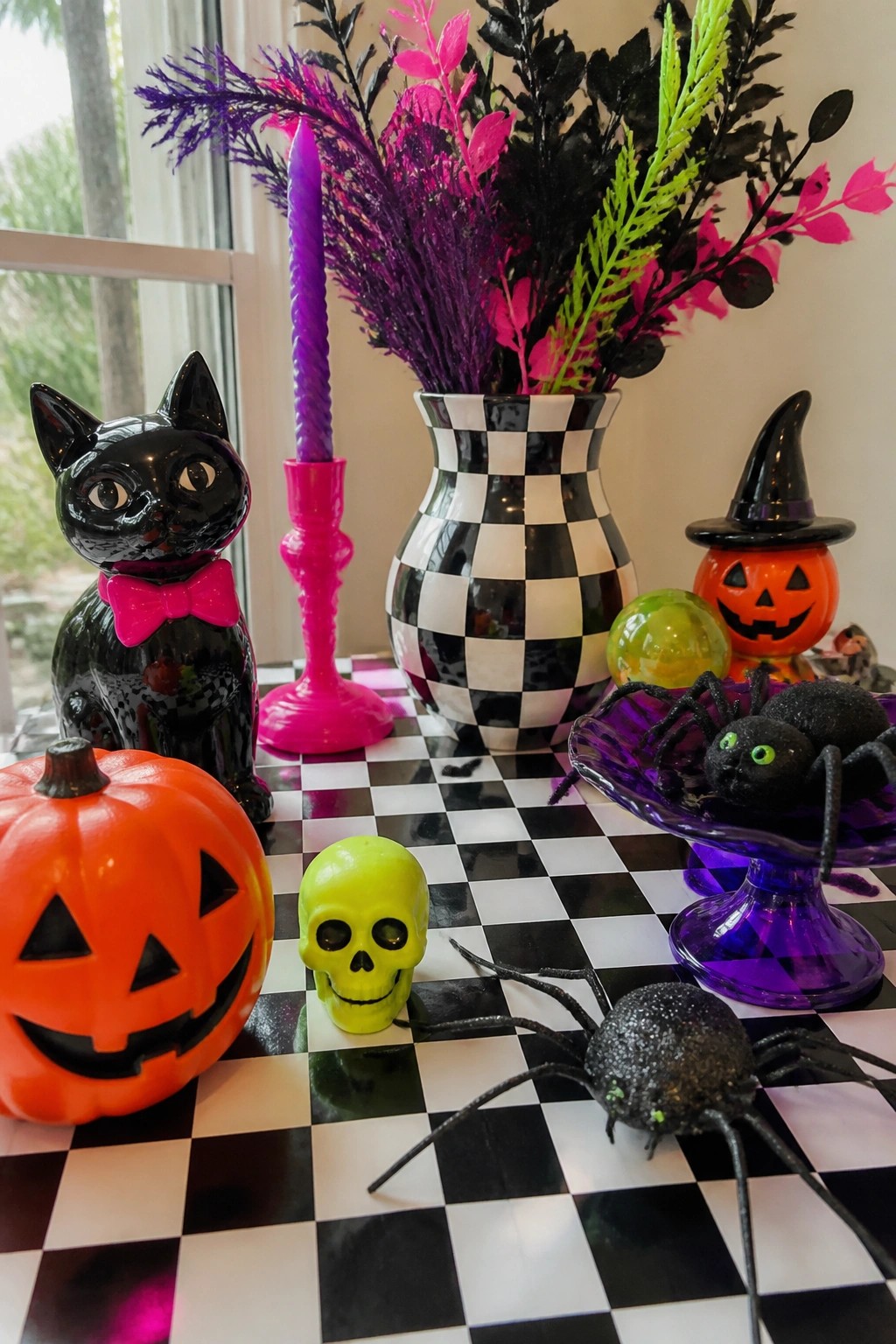 Halloween decorations with black cat, pumpkins, skull, spiders, candle, and checkered vase on table