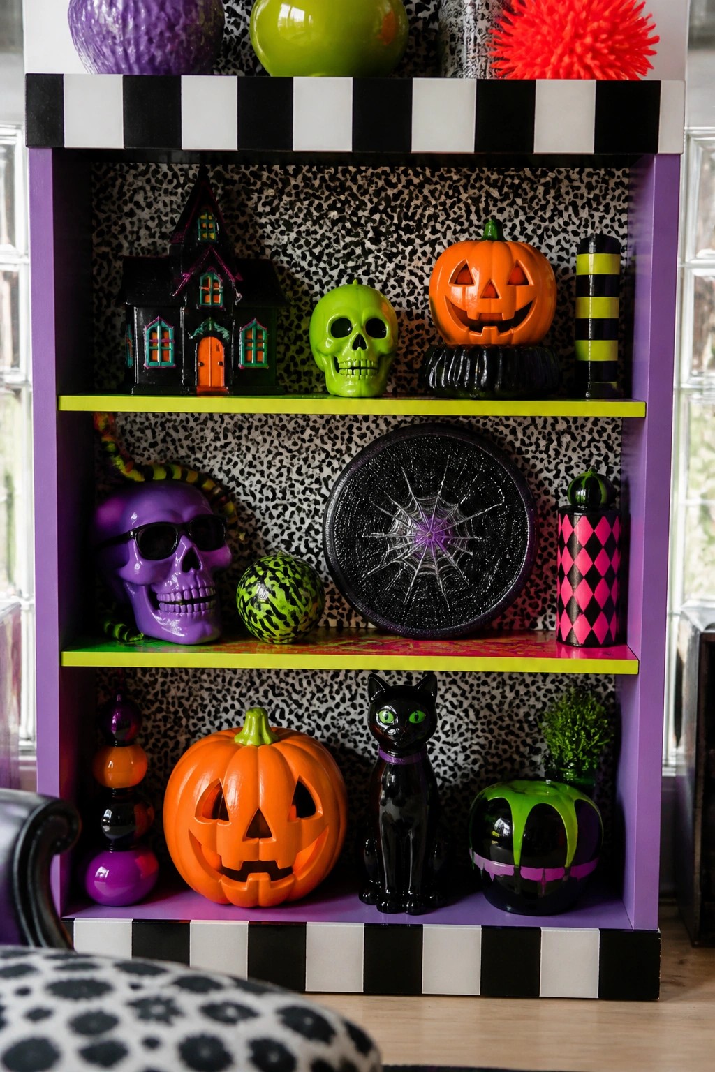 Purple open shelves styled with retro Halloween decorations including skulls, jack o lanterns, a black cat, and a spiderweb plate.