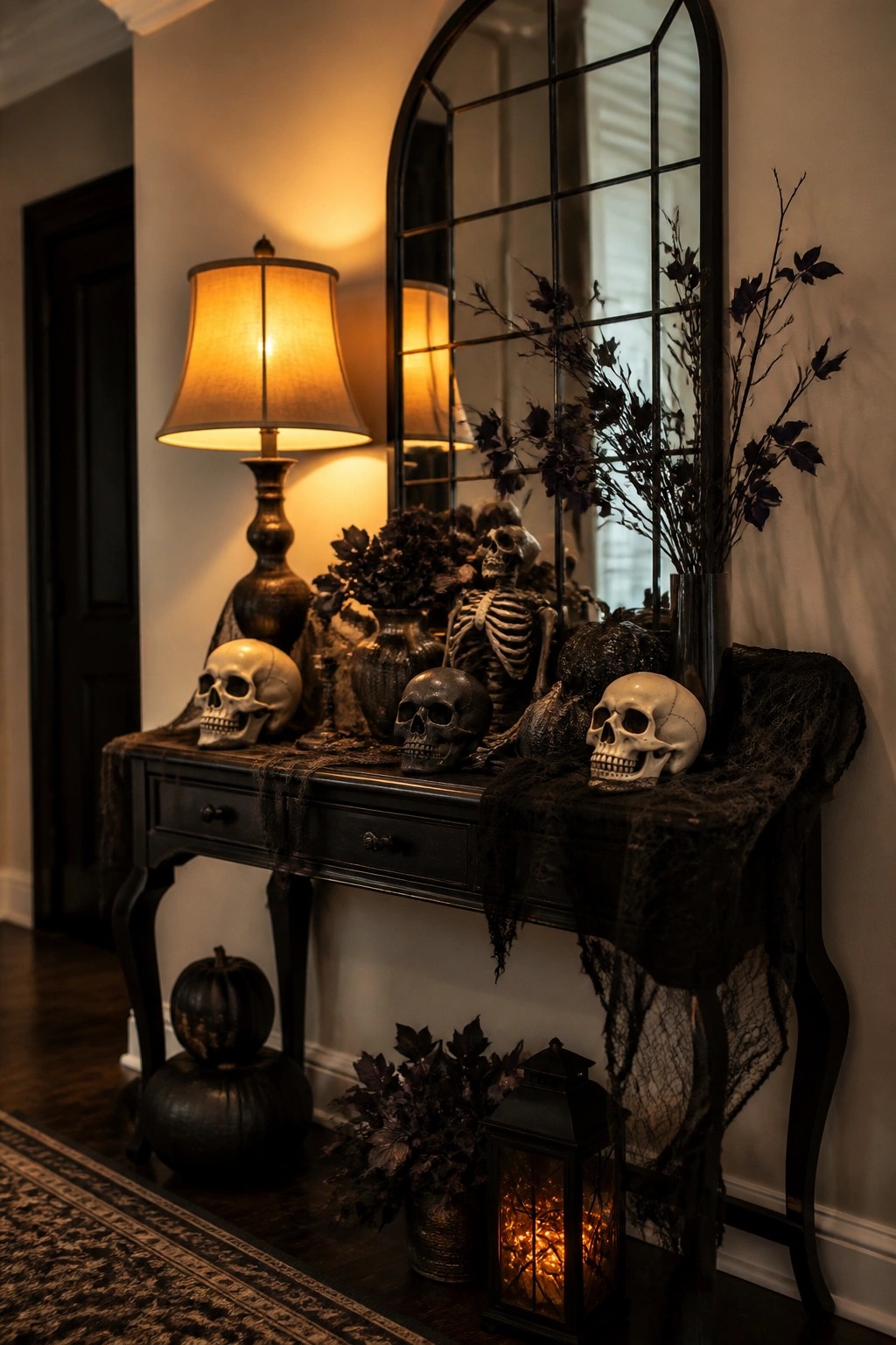 Entryway console table styled with multiple skulls, a small skeleton figure, black branches, and dark fabric beneath a large mirror.