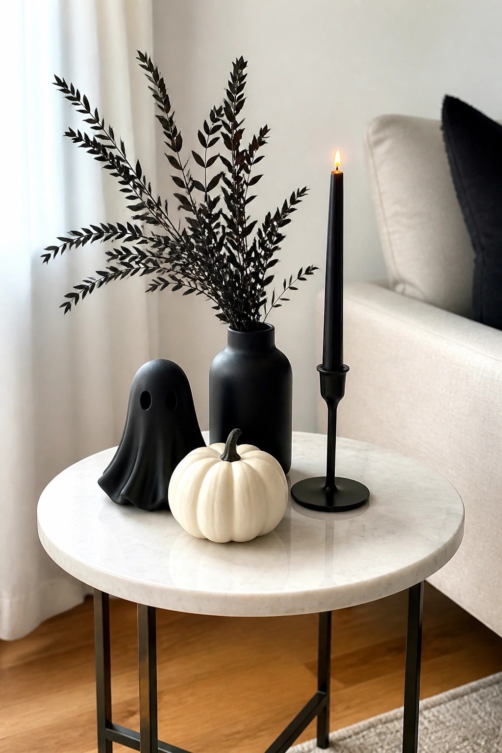 Small round marble table holding a black ghost figurine, white pumpkin, black vase with dark branches, and a lit black taper candle.