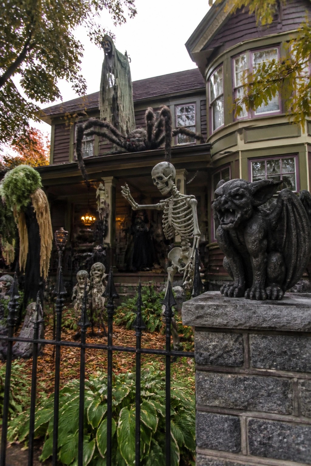 Halloween-decorated house with waving skeleton, giant spider, gargoyle, and creepy dolls.