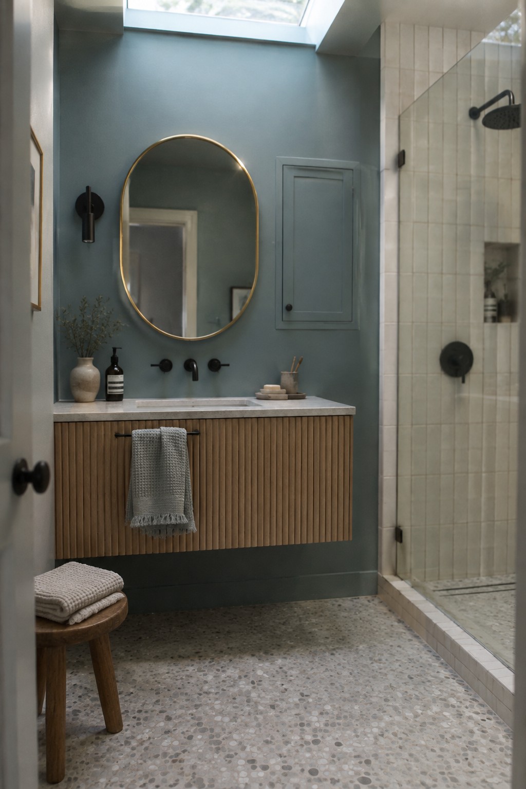Muted blue-green bathroom walls above a warm wood vanity beside a tiled shower.
