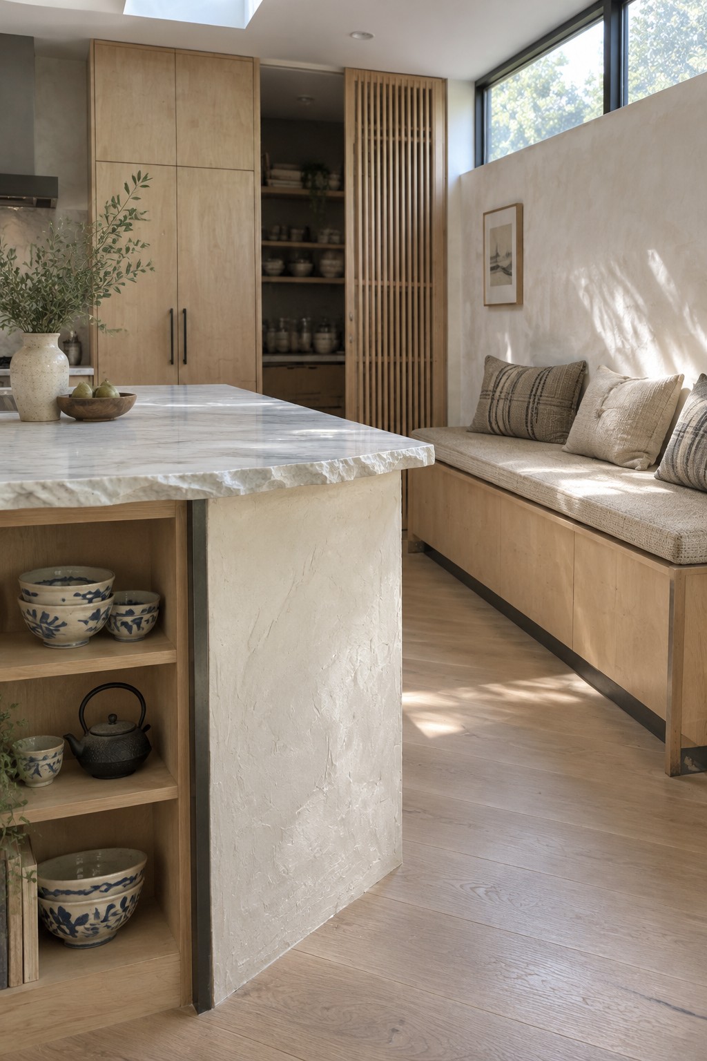 A wood kitchen island sits beside a built-in bench with beige cushions and tall wood cabinets.