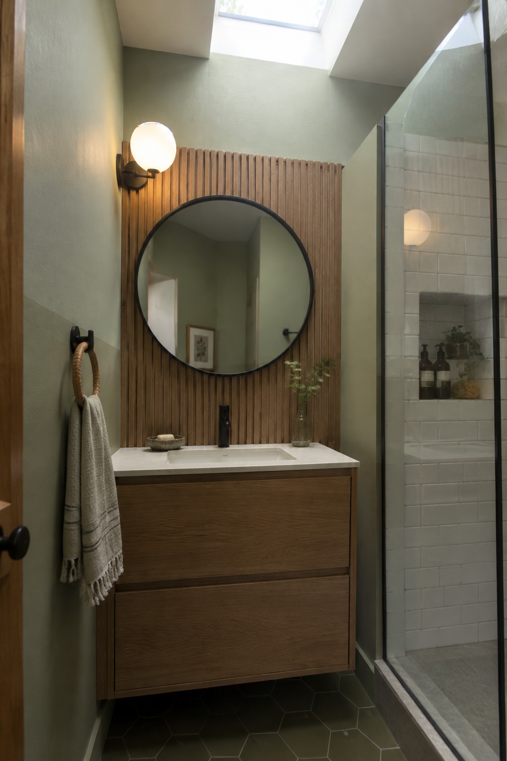 Soft sage green walls in a small bathroom with white shower tile and dark hexagonal flooring.
