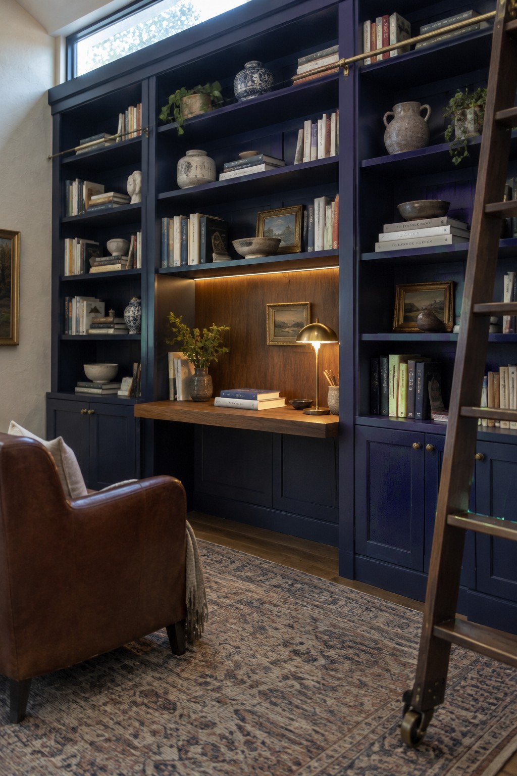 Deep blue-black built-in bookshelves surround a walnut desk in a home study.