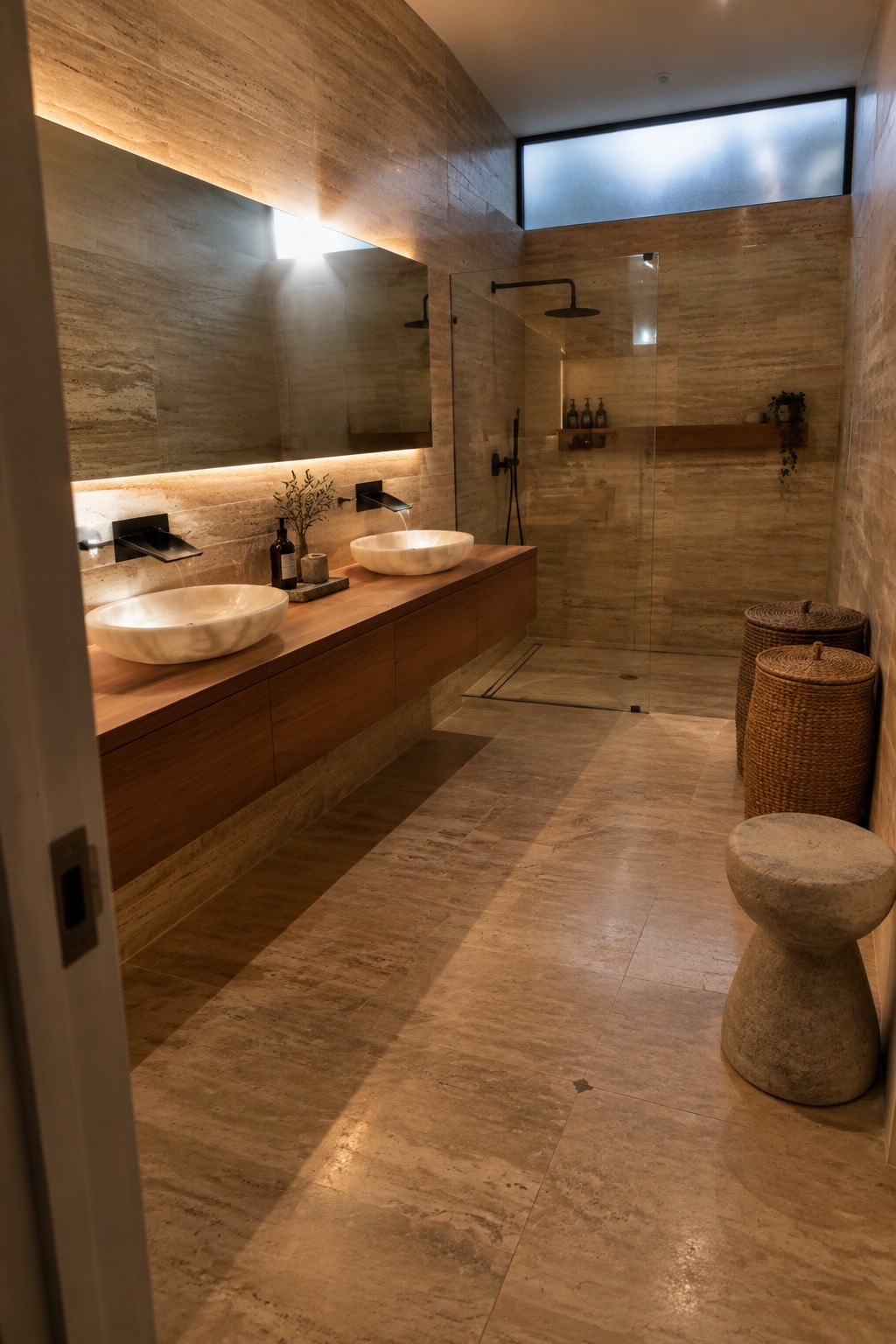 A bathroom with stone walls and floor, a floating wood vanity with two vessel sinks, and a glass shower enclosure.