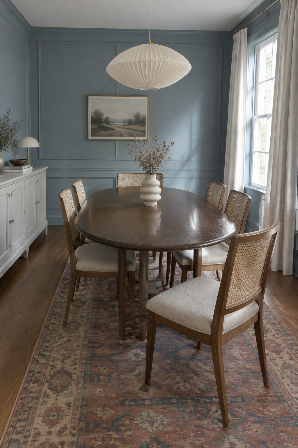 Muted blue-gray paint covers the paneled walls of a dining room with dark wood floors and a table.